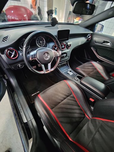 Interieur van een auto met zwarte bekleding en rode accenten, dashboard en stuur zichtbaar.